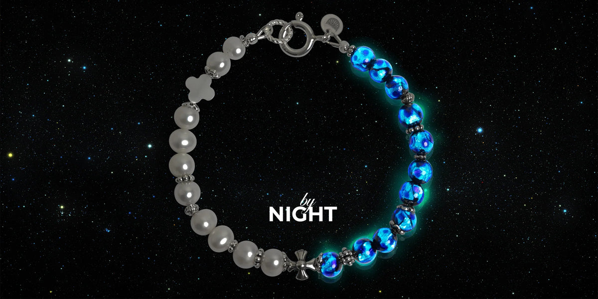 The DAÏQUIRI GLOW MIDNIGHT Bracelet at night: its Hotaru beads glow blue-green beside freshwater cultured pearls against a starry sky, with the words by NIGHT