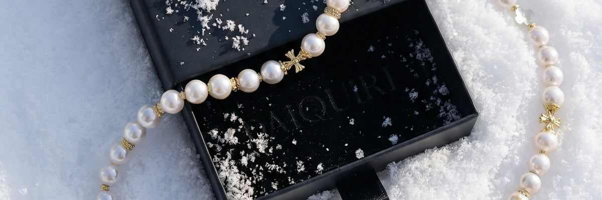 Collier de perles de culture blanches à croix dorées posé sur un écrin noir DAÏQUIRI ouvert, dans la neige