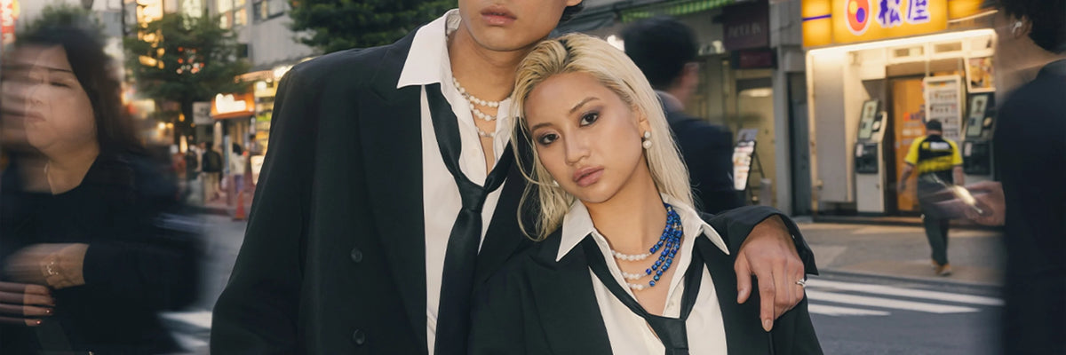 Deux mannequins en blazer noir et cravate, colliers de perles au cou, dans la rue