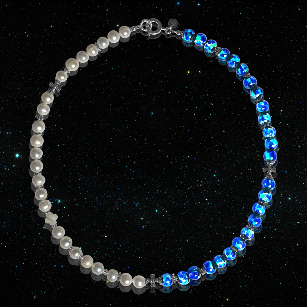 Le Collier DAÏQUIRI GLOW MIDNIGHT sur fond de ciel étoilé : d’un côté les perles de culture d’eau douce, de l’autre les perles Hotaru bleues, avec un quatre-feuilles en nacre et des croix en argent
